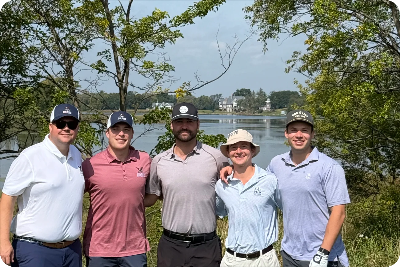 Five golfers posing near a lake with trees in the background