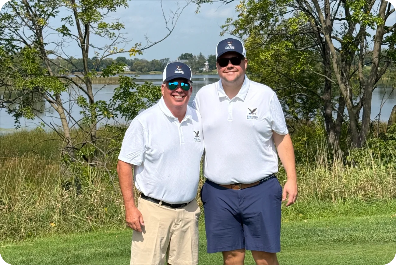 Two men in Bird Bottle Open polo shirts posing near a lake