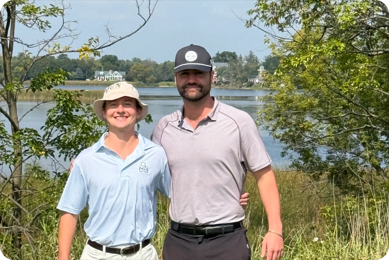 Two men smiling together on a golf course near a lake