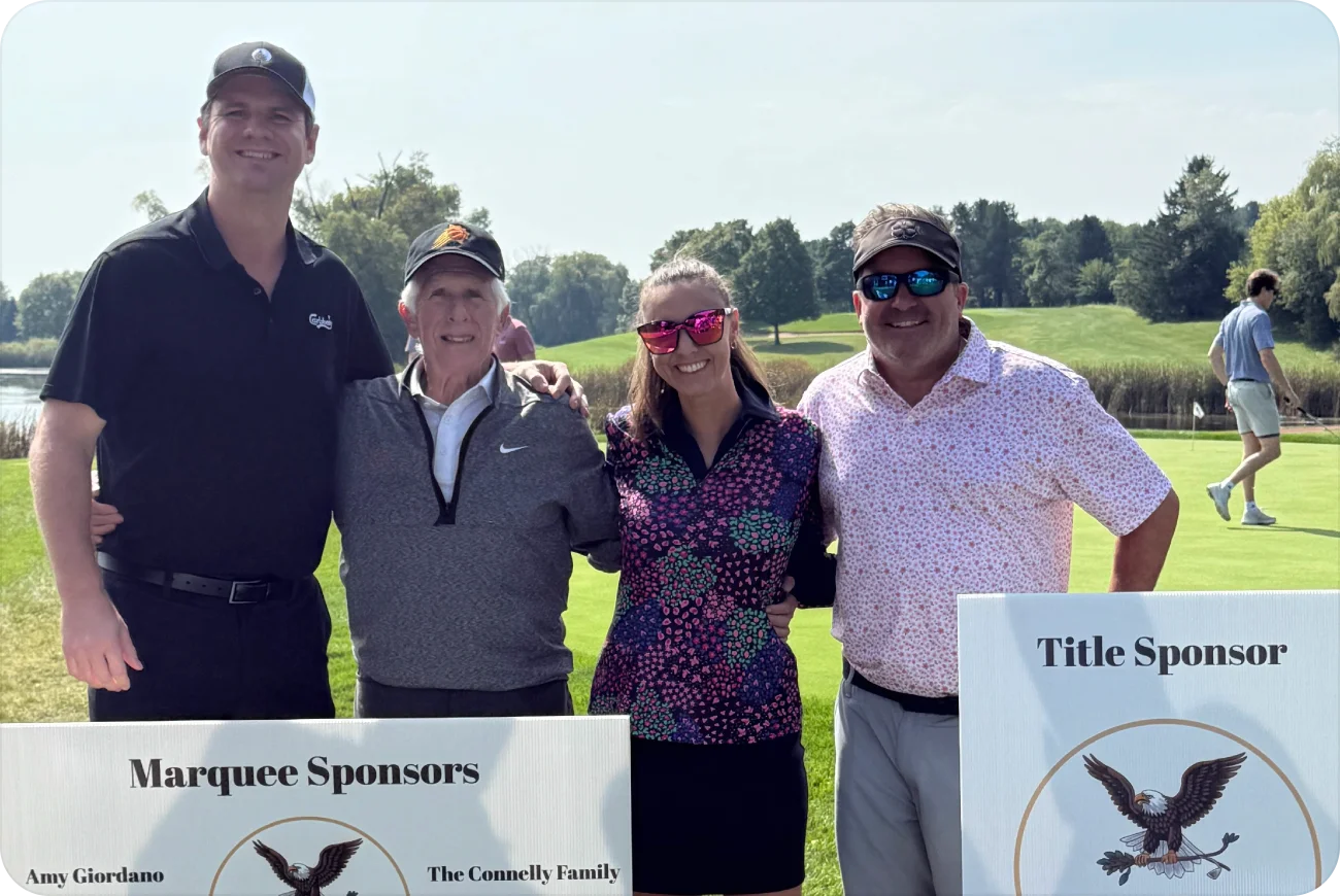 Four golfers posing next to event sponsor signs on a sunny course