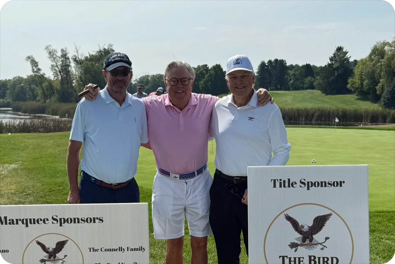 Three men posing next to Marquee Sponsors and Title Sponsor signs on the fairway