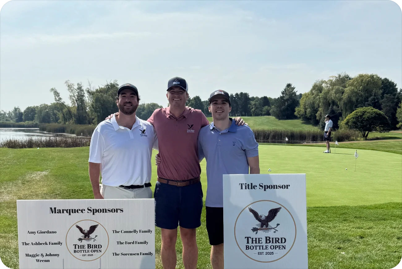 Three men posing with Bird Bottle Open sponsor signs on the golf course