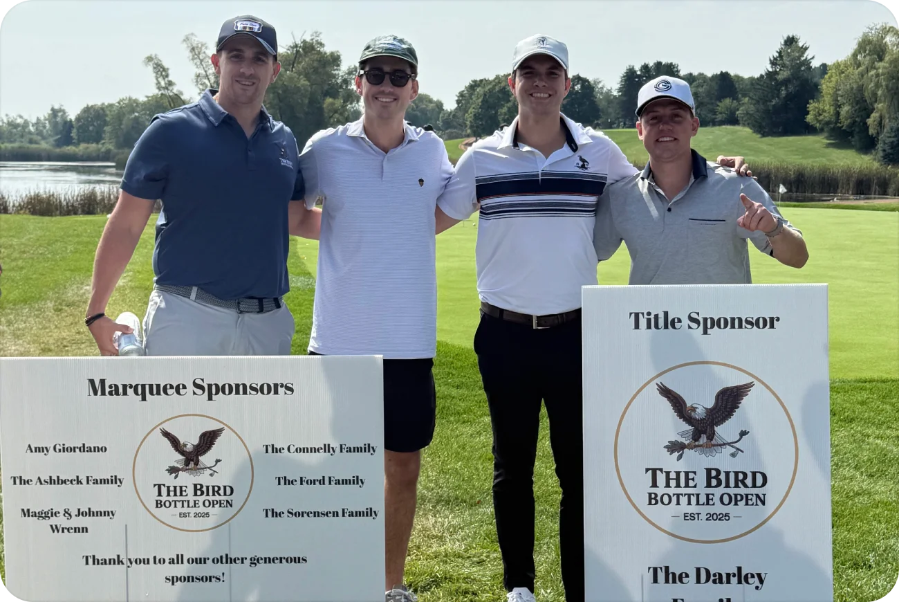 Four men posing next to Marquee Sponsors and Title Sponsor signs
