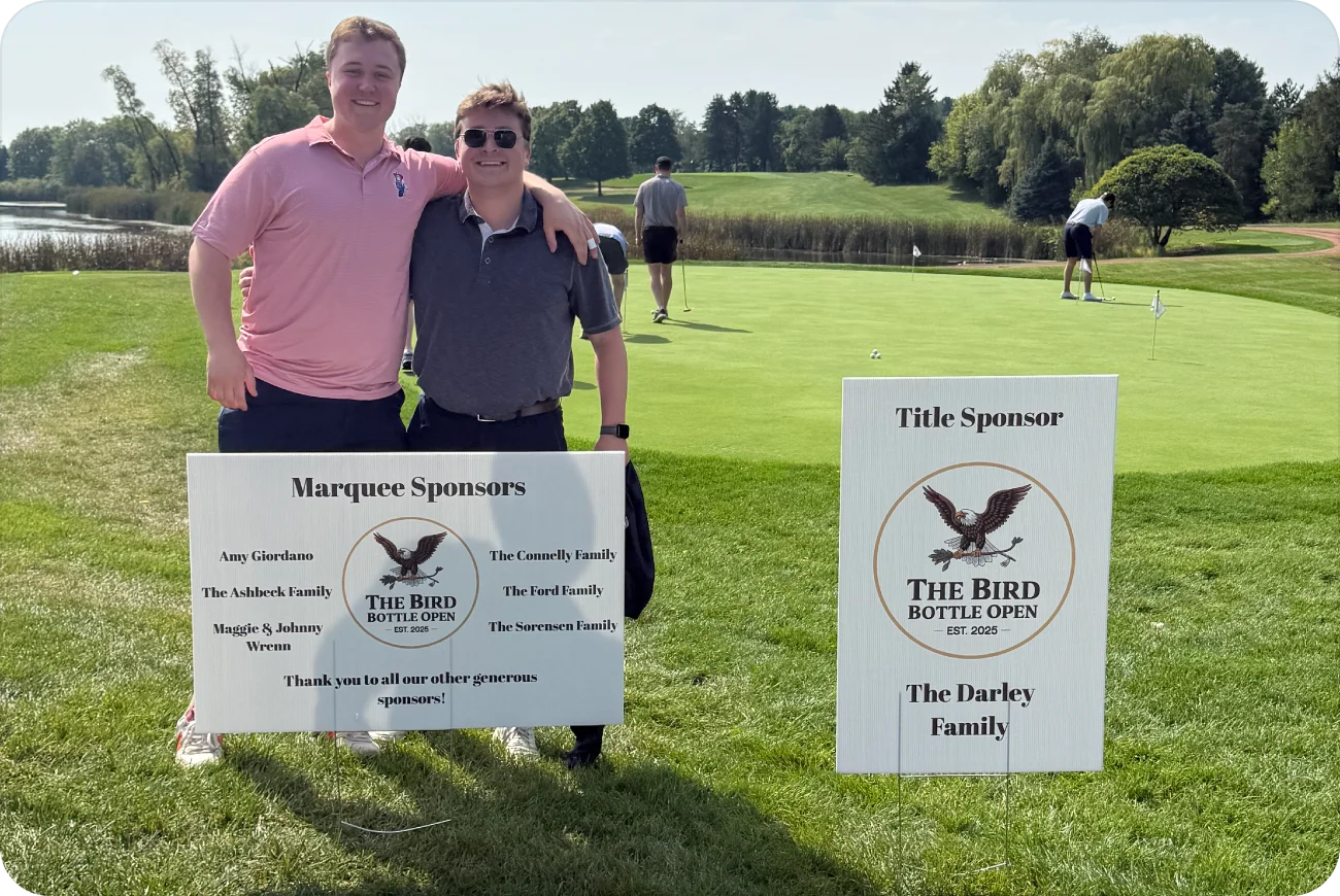 Two golfers posing next to sponsor signs near the clubhouse