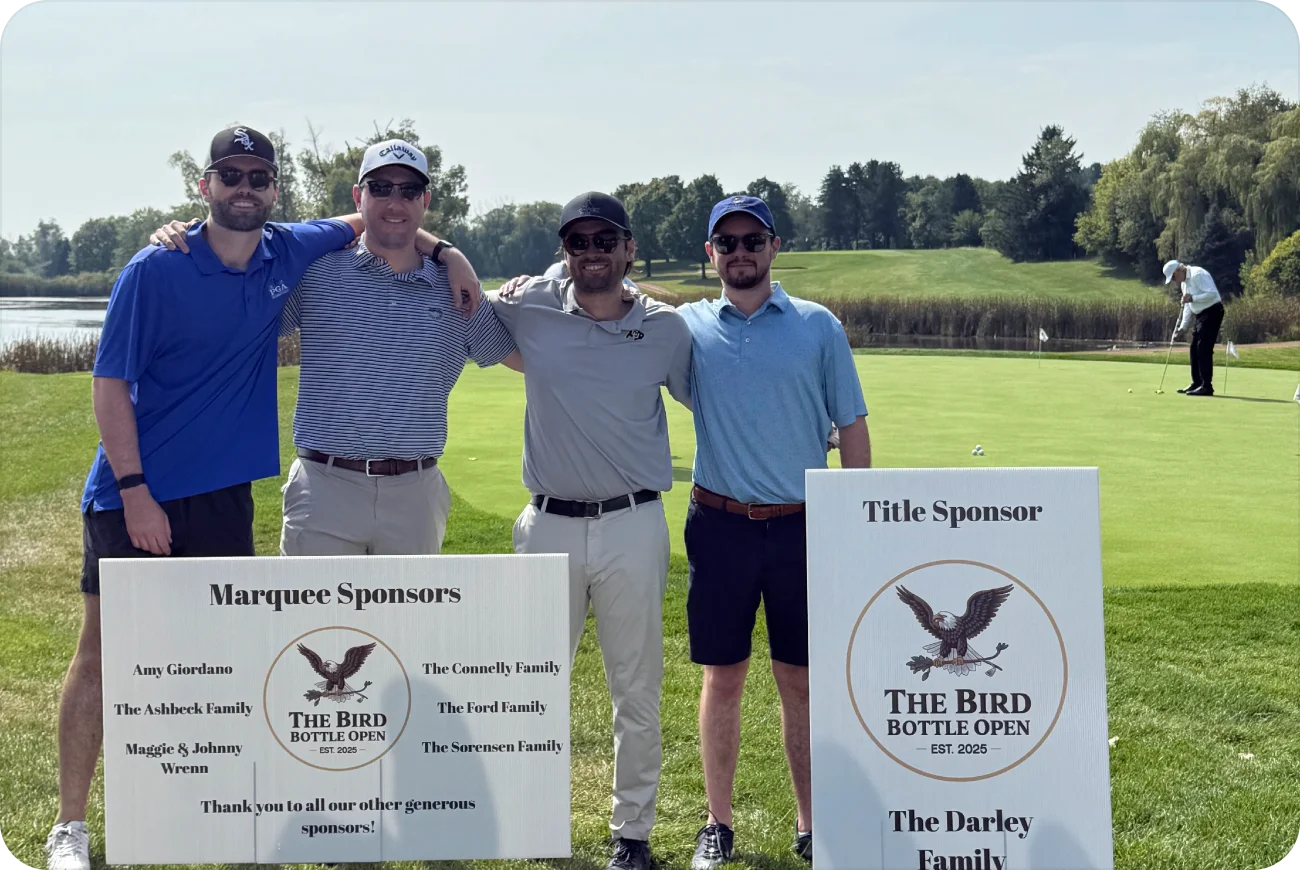 Four men posing next to Marquee Sponsors and Title Sponsor signs on the course