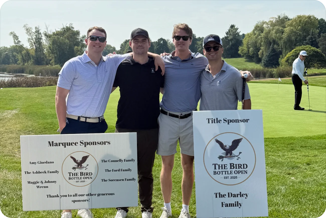 Four men posing next to the Bird Bottle Open Marquee and Title Sponsor signs