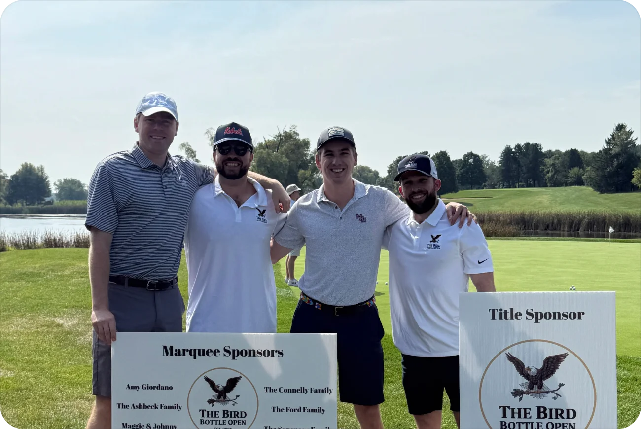 Four men smiling next to Marquee and Title Sponsor signs on a sunny fairway