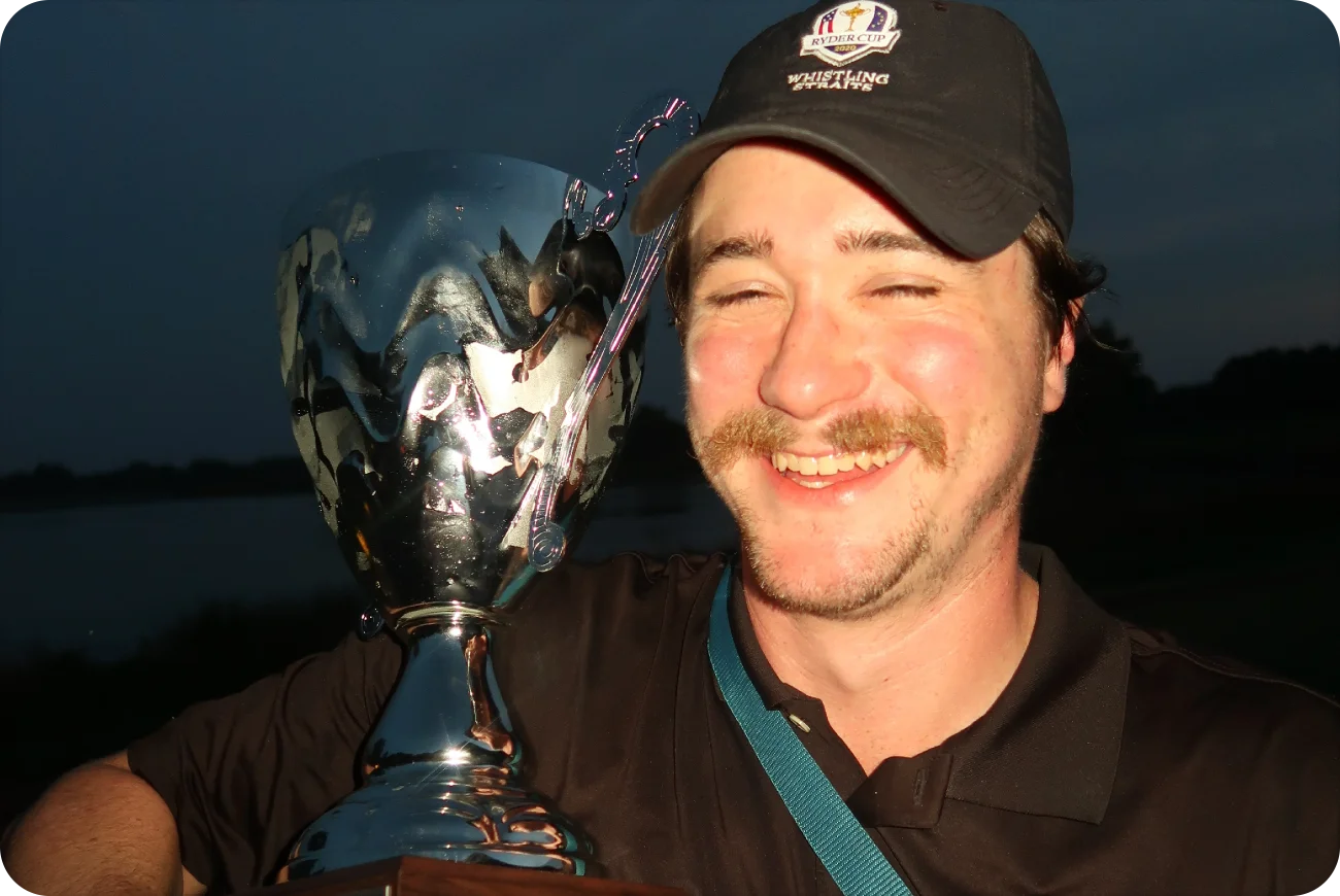 Man smiling and holding the Bird Bottle Open championship trophy at night