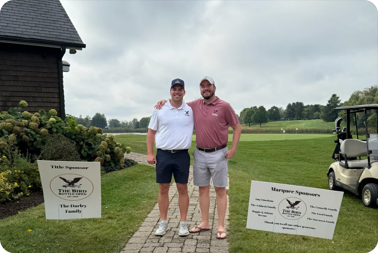 Two men posing together next to sponsor signs near the clubhouse