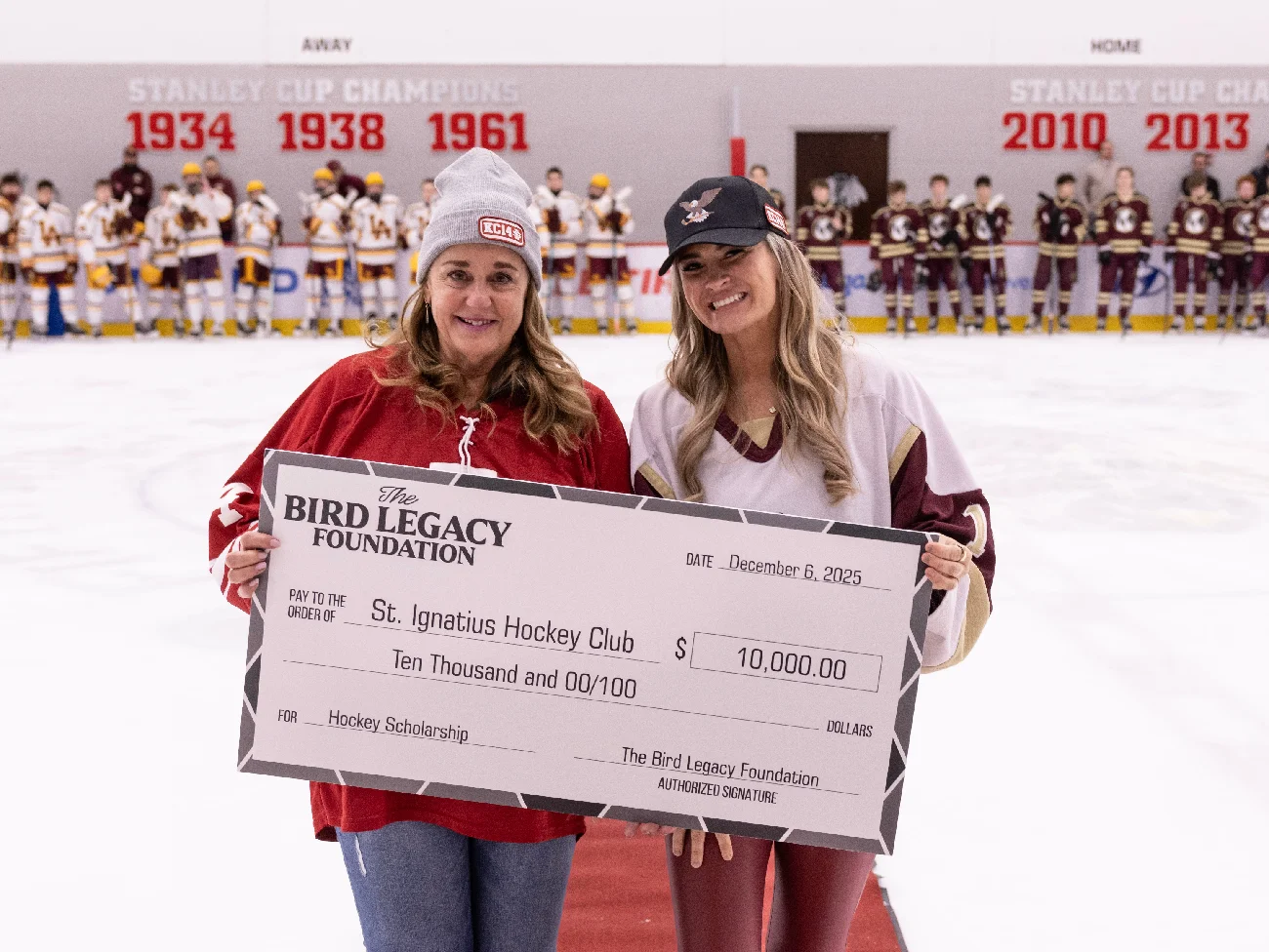 Two women on the ice presenting a $10,000 scholarship check from the Bird Legacy Foundation