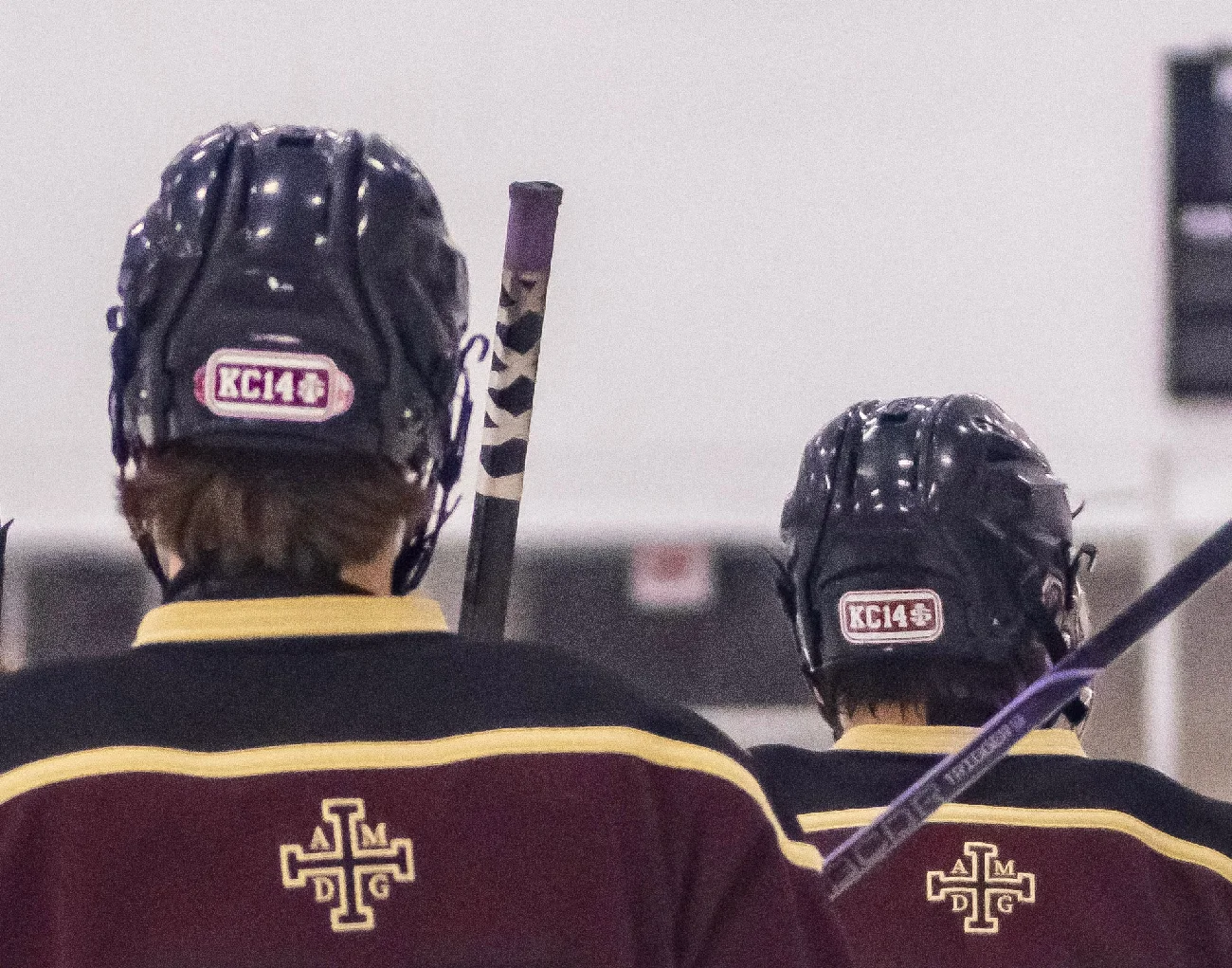 Two hockey players wearing helmets with KC14 memorial stickers on the back