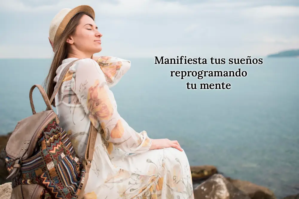 Mujer sentada en la orilla del mar con los ojos cerrados y expresión serena, simbolizando introspección y el proceso de manifestar sueños reprogramando la mente