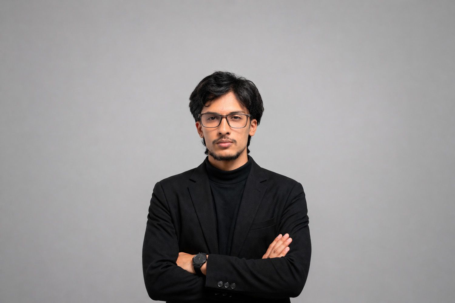 Professional portrait of Bishal Giri in a black blazer and turtleneck, arms crossed, grey studio background