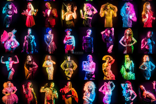 An array of drag queens side-lit in different colours on a black background