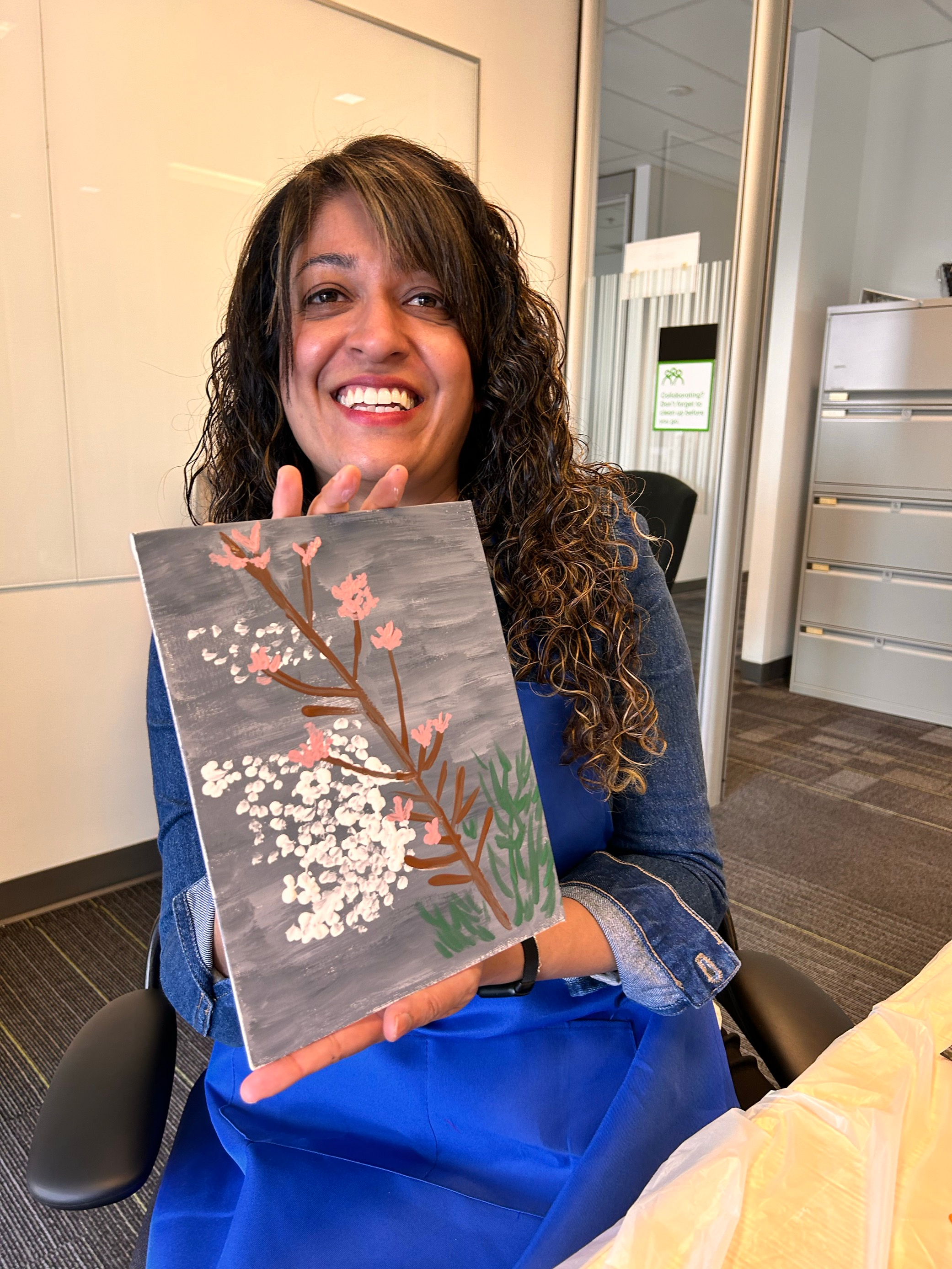 Smiling woman proudly shows painted piece of a pink blossom branch against a river current backdrop.