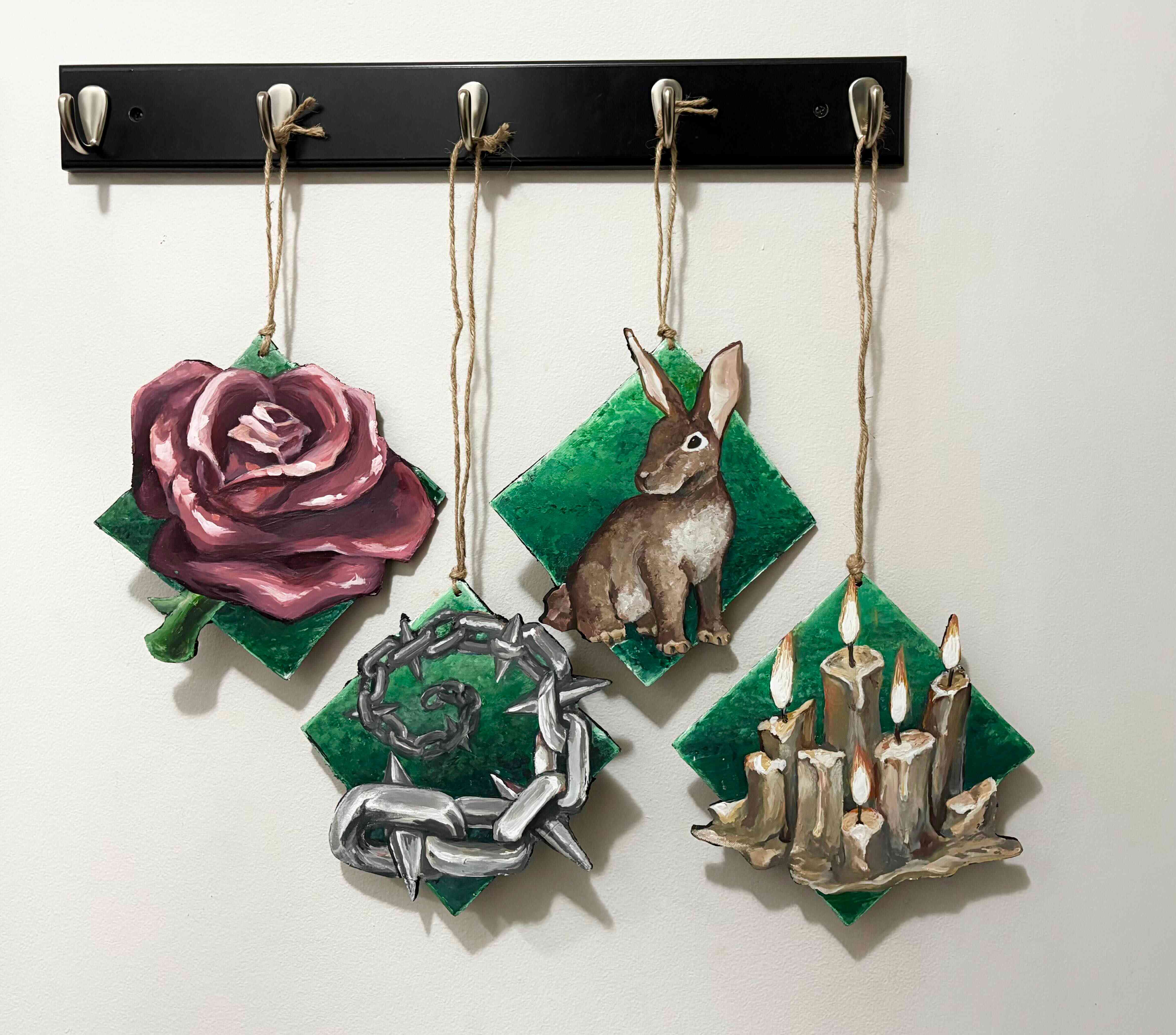Four ornamental signs hanging from a coat rack featuring a rose, spiked chains, rabbit, and groups of candles. Reference inspired from Crusader Kings 3, attribution to Paradox Interactive.