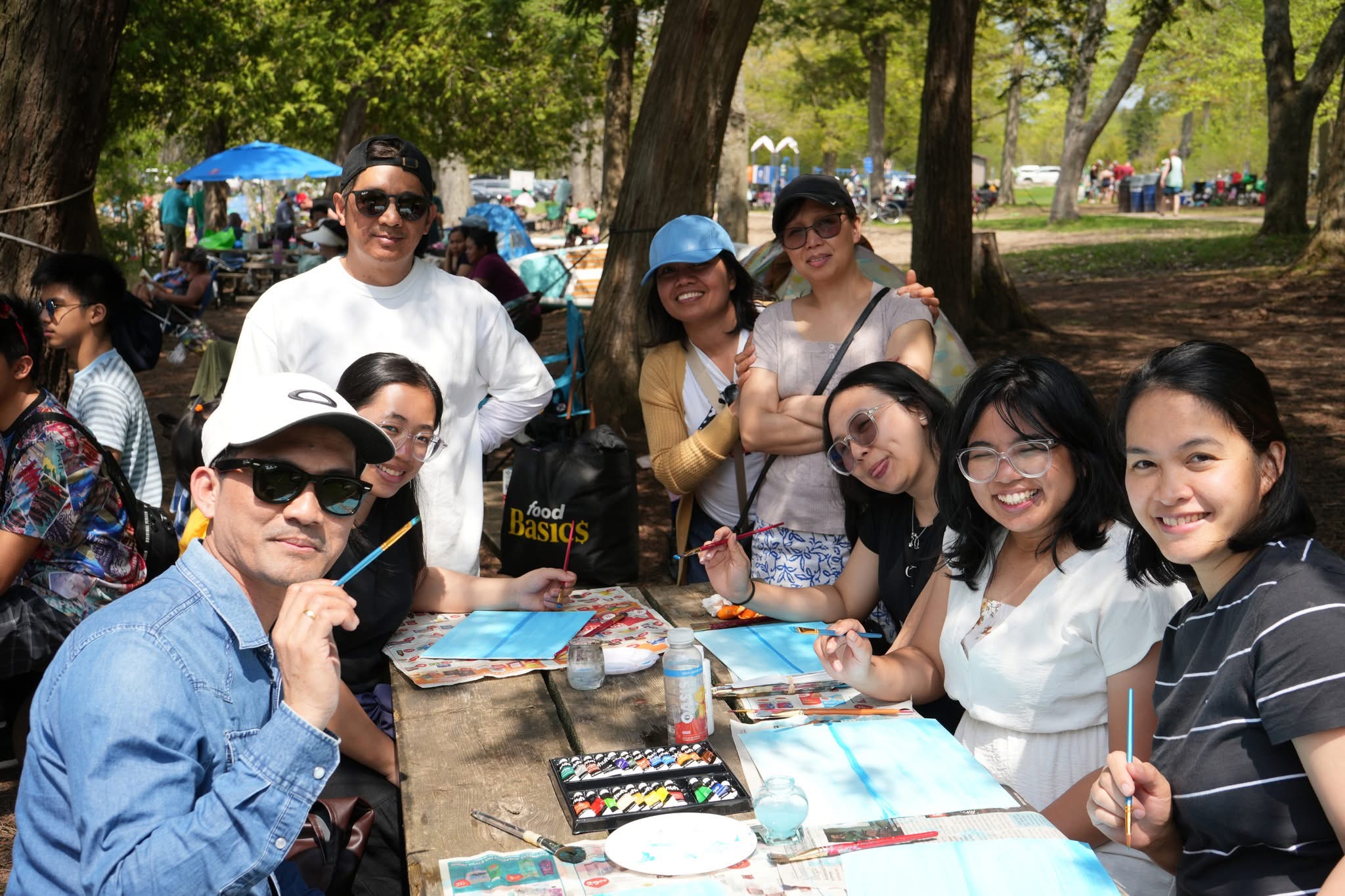 A live pop up class by the lake with people painting on canvases and an instructor demonstrating techniques.
