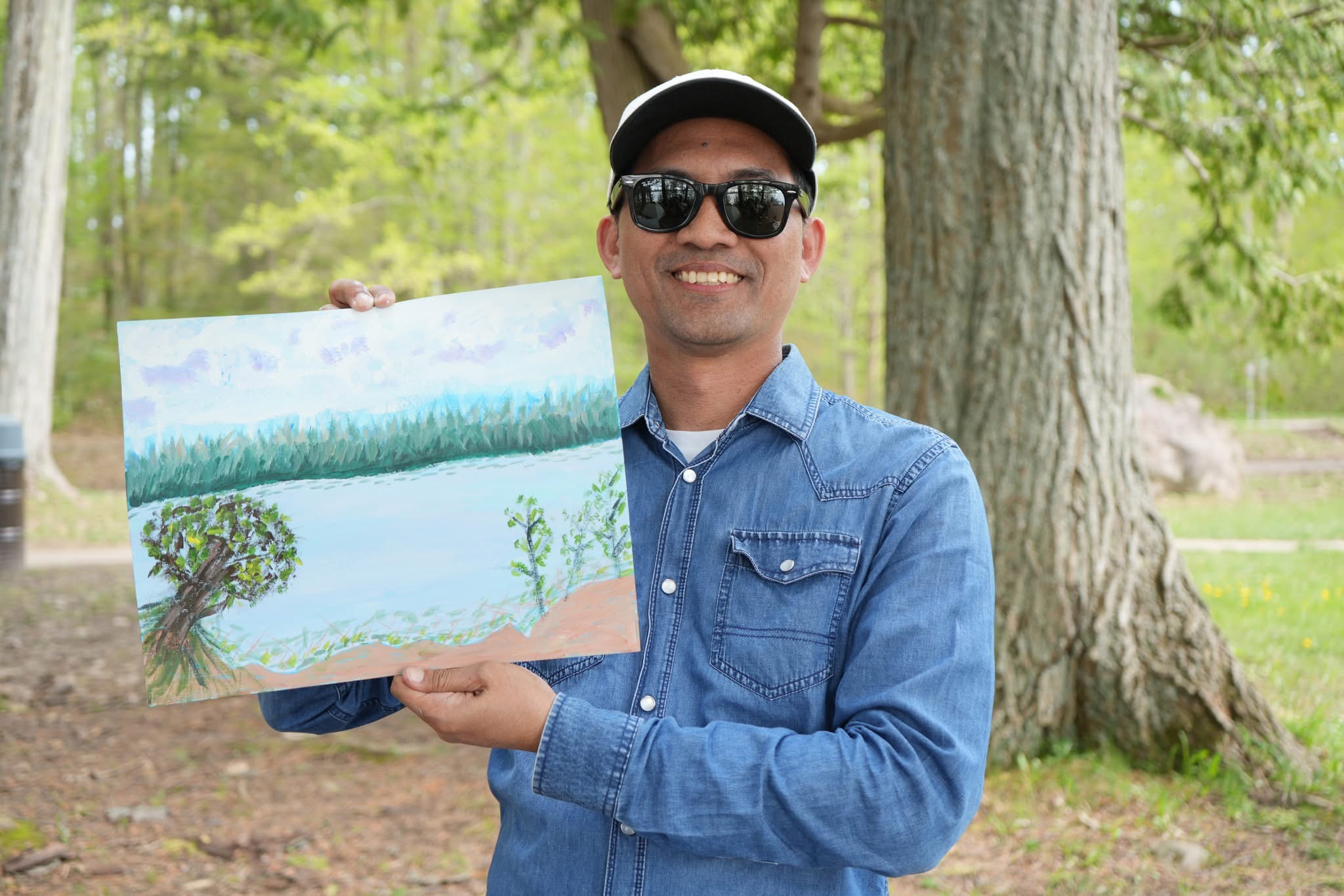 Tito shows his finished painting of a lake scene with trees and woods in the background.