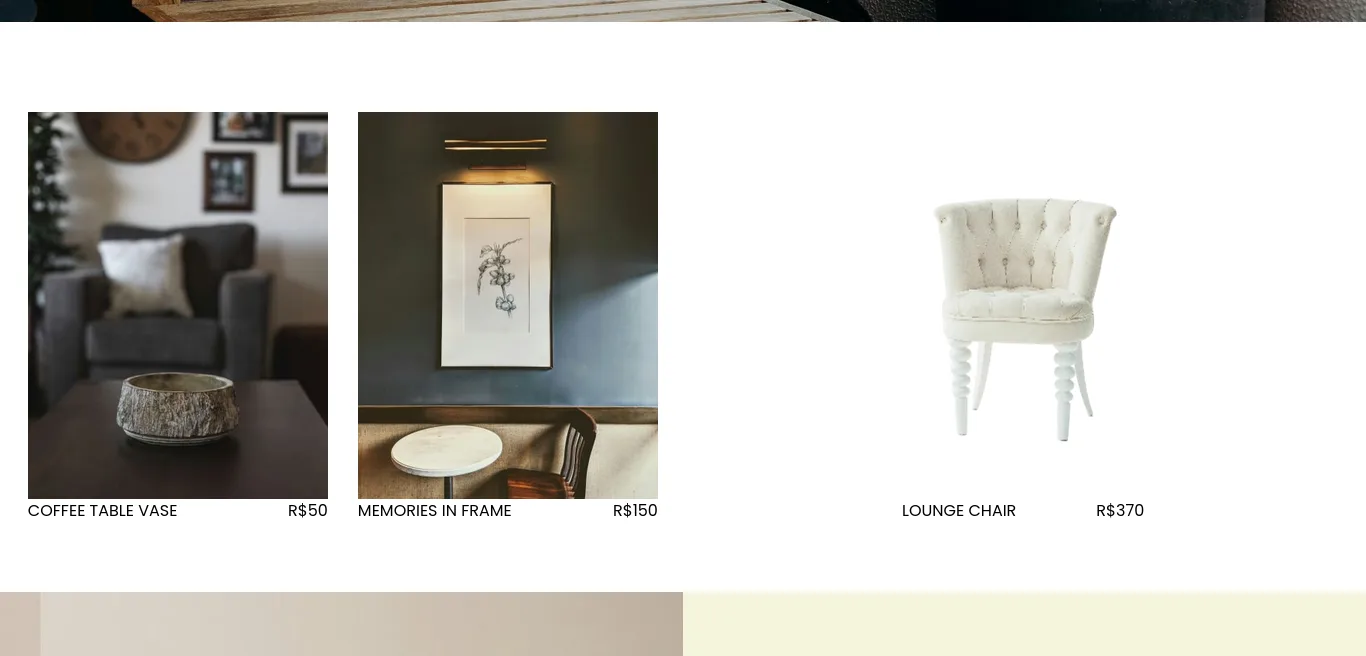 A clean, minimalist product grid section on the Woode website featuring three items. From left to right: 'COFFEE TABLE VASE' (R50), showing a textured stone bowl on a dark wood table in a cozy living room context;′MEMORIESINFRAME′(R150), displaying a framed botanical print on a dark wall illuminated by a picture light; and 'LOUNGE CHAIR' (R$370), featuring a white button-tufted chair with ornate spindle legs on a plain white background. The layout uses uppercase typography for titles and clear pricing.