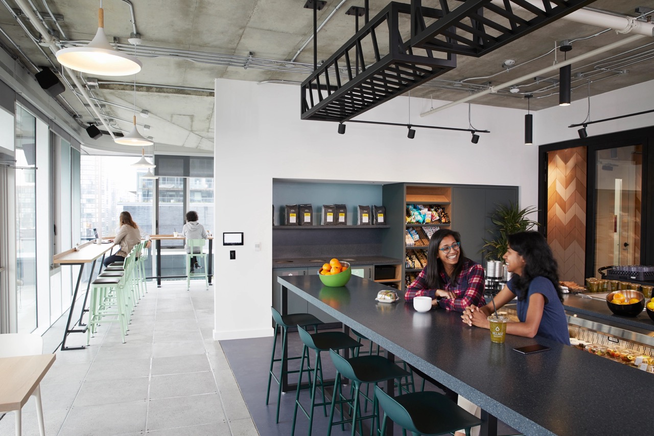 People working at tables in a kitchen-style area in an open office.