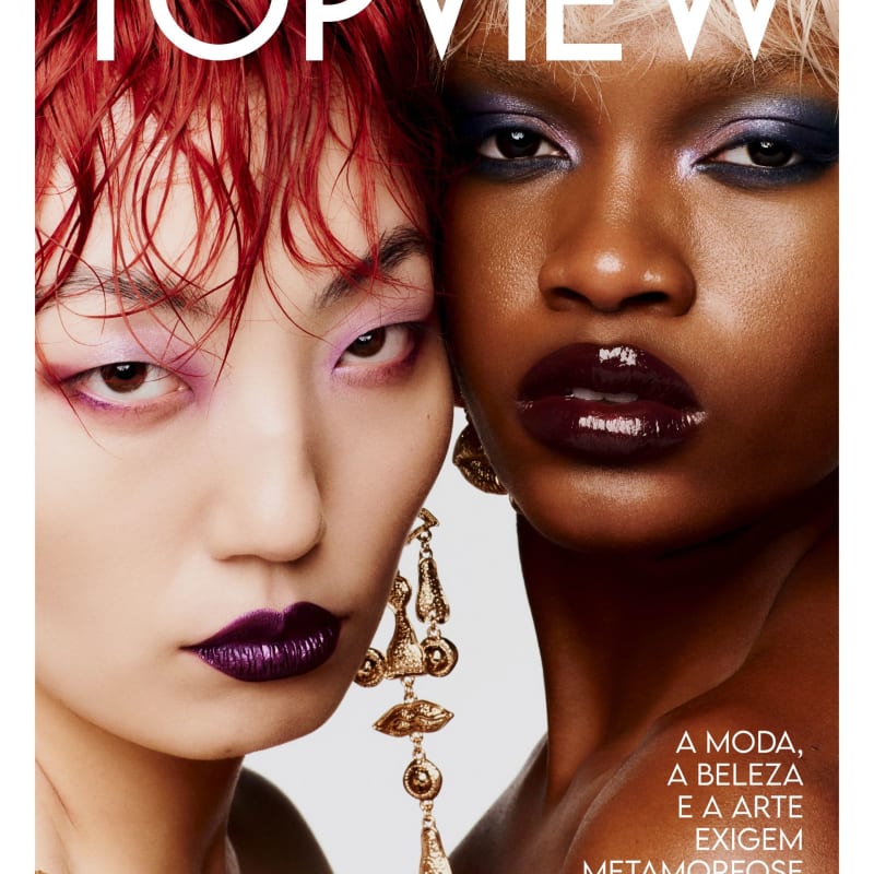 Close de duas modelos com maquiagem marcante, uma ruiva e outra negra, lado a lado em fundo claro