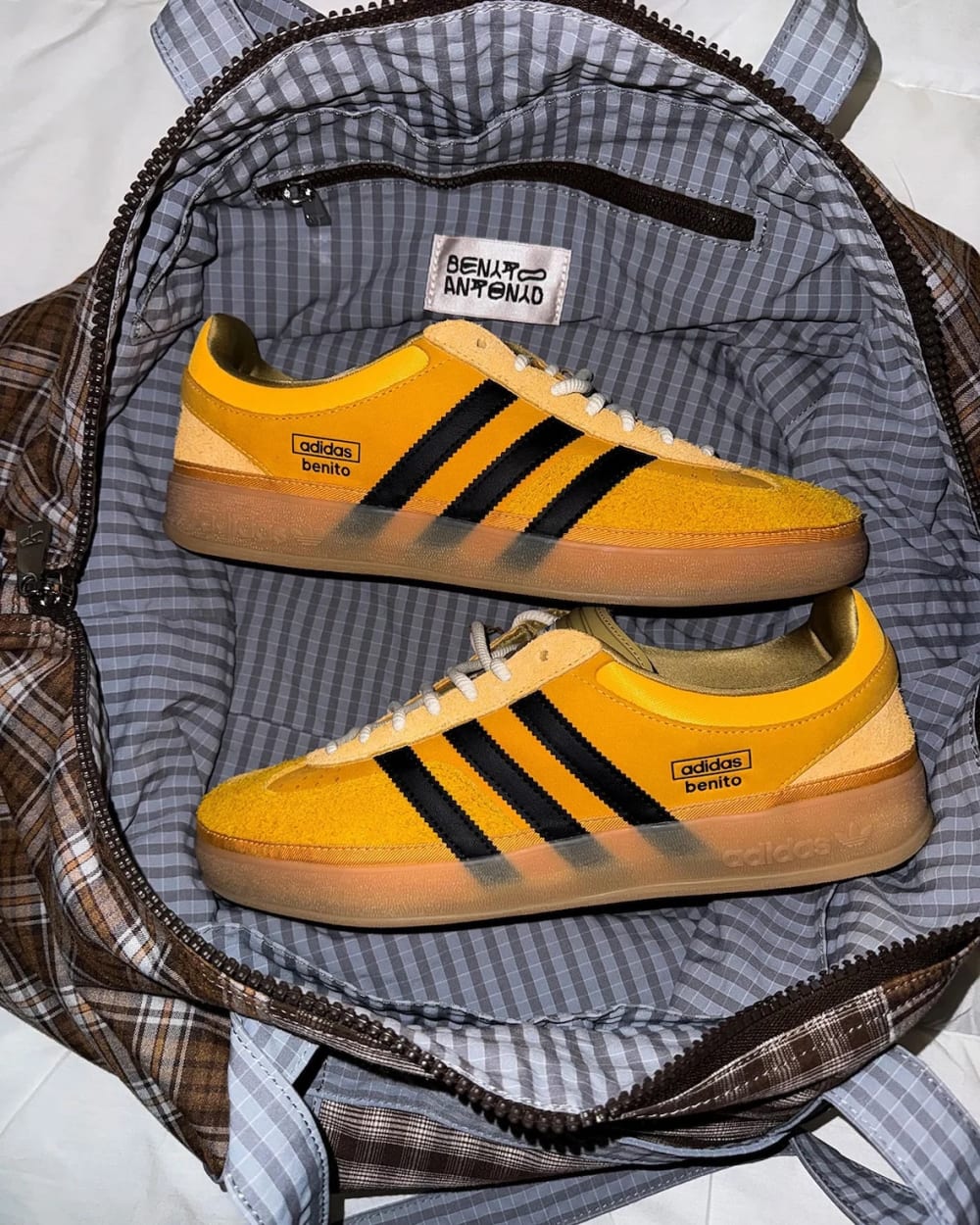 Bad Bunny adidas Gazelle Indoor Solar Gold KI2592 yellow suede pair resting in a plaid duffel bag with Benito Antonio label