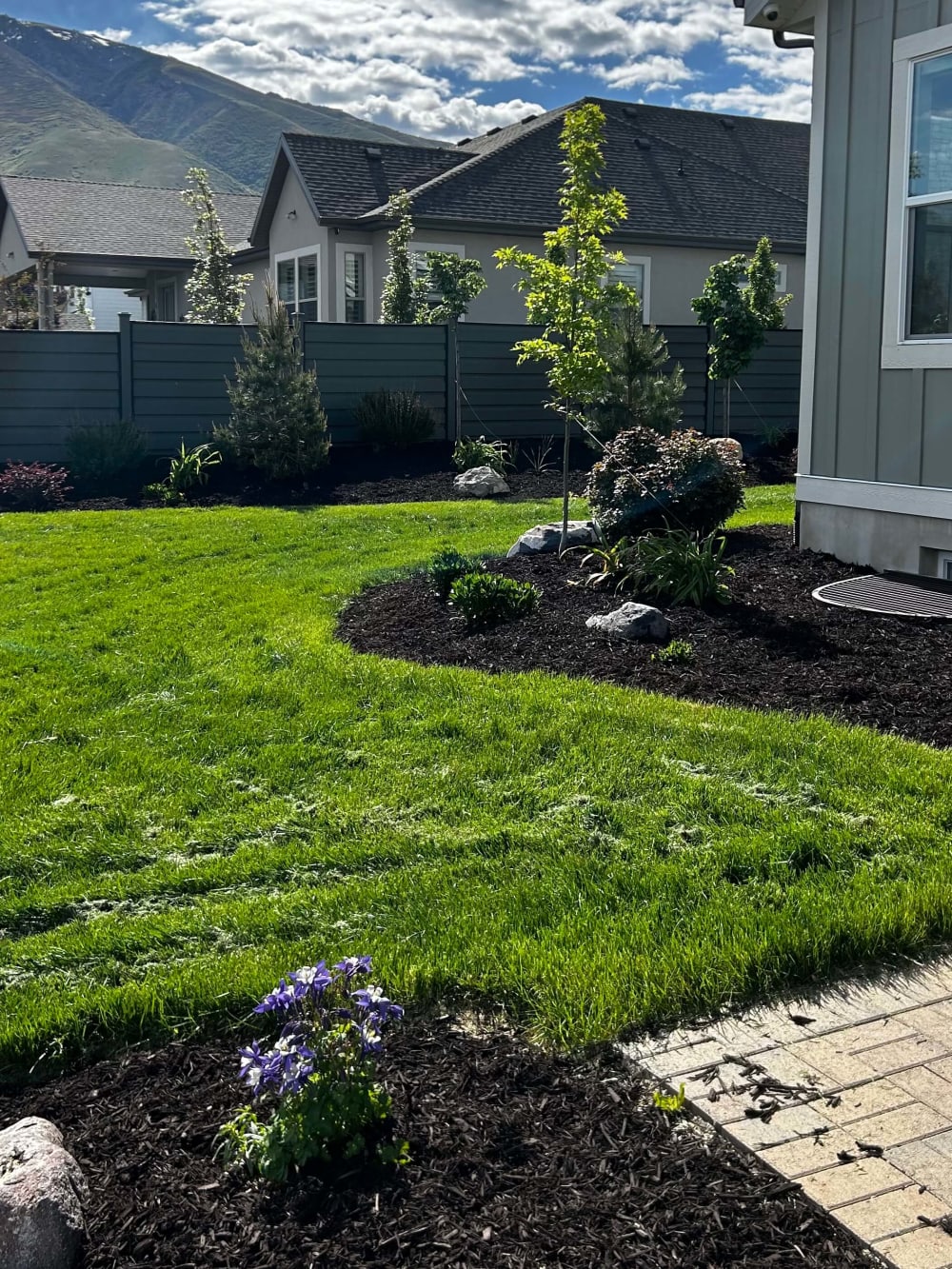 Finished lawn, curved planting beds, and a paver walkway with Utah mountains in the background