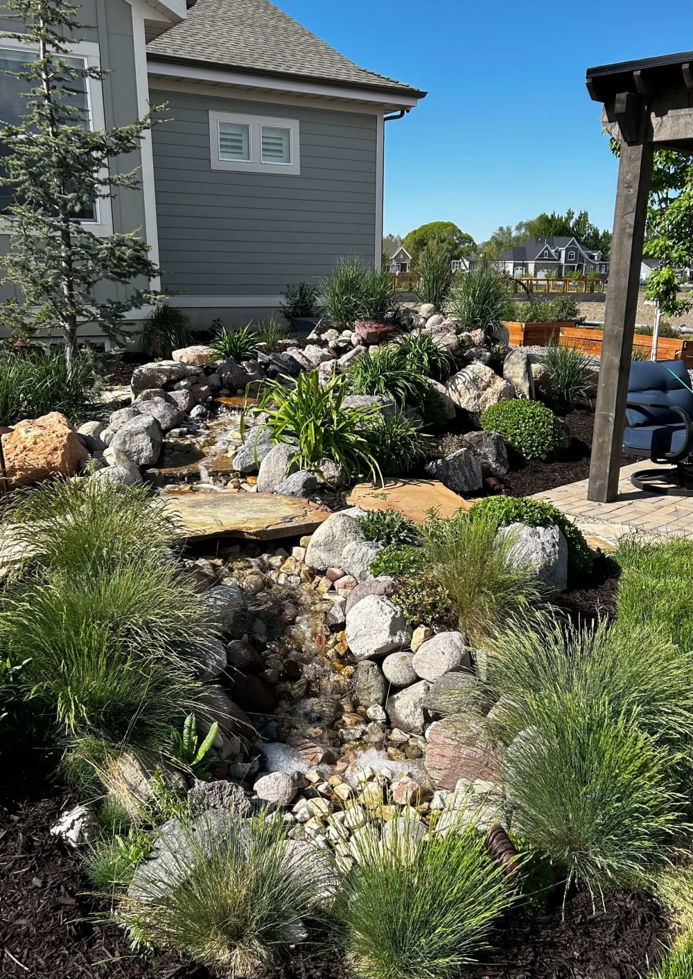 Rock-lined backyard stream surrounded by ornamental grasses and planting beds