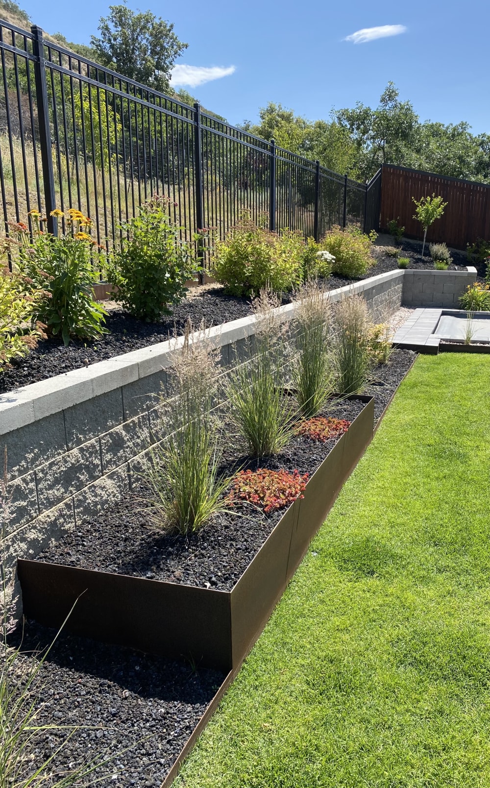 Tiered retaining wall and planting beds below a black metal fence