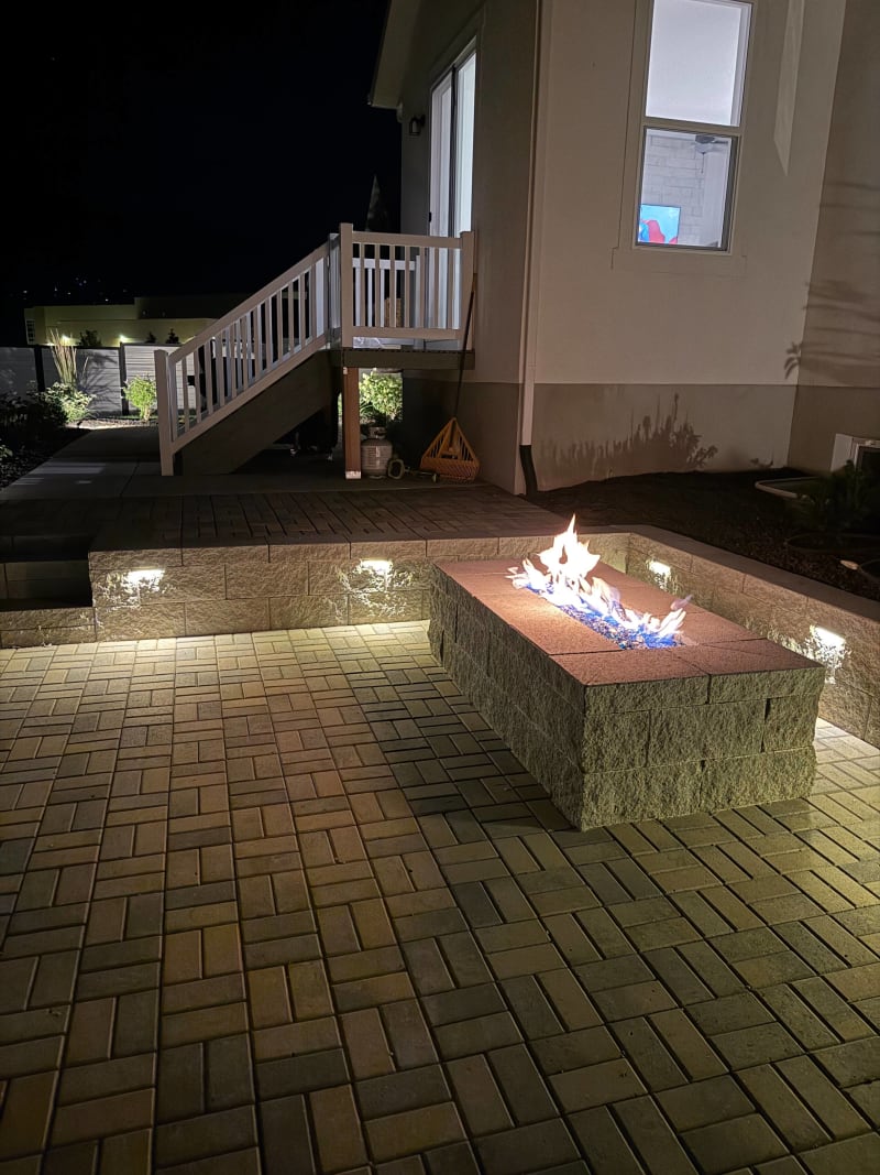 Illuminated paver patio, built-in fire pit, and steps at night