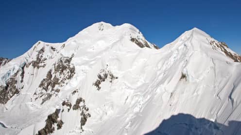 Rarakiroa Mount Tasman |  - Majestic snow-capped mountain peaks rise against a brilliant blue sky, casting dramatic shadows on the surrounding terrain. 1