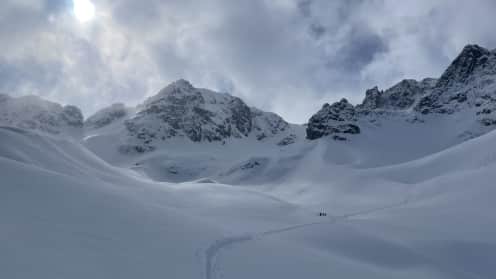  Off the Grid in the Cass | Four days of backcountry ski touring from Lady Emily Hut - A vast, snow-covered landscape with towering, rugged mountains in the background, and a set of footprints leading across the snowy expanse in the foreground. 1