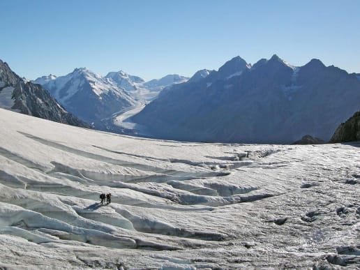 New Zealand Alpine Hikes, Trekking & Snowshoeing - Trans-Alpine Crossings & Traverses - Ball Pass Crossing - Ball Pass - Ball Glacier crevasses - A vast, snow-covered glacier stretches out in the foreground, surrounded by towering, jagged mountain peaks in the background under a clear, blue sky. 9