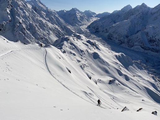 New Zealand Backcountry Skiing & Split-boarding - New Zealand's Best Glacier Touring & Ski Mountaineering - Ski Mount Cook Range - Ski touring above Caroline Hut, Tasman Valley, Aoraki Mount Cook National Park - Ski tourers traverse a snow-covered mountain landscape, surrounded by towering, rugged peaks in the background. 2
