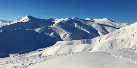 Heli Ski & Split-board Tours - Heli-assisted Ski & Split-board Tours - Majestic snow-capped mountains rise against a brilliant blue sky, with a snowy landscape in the foreground. 1
