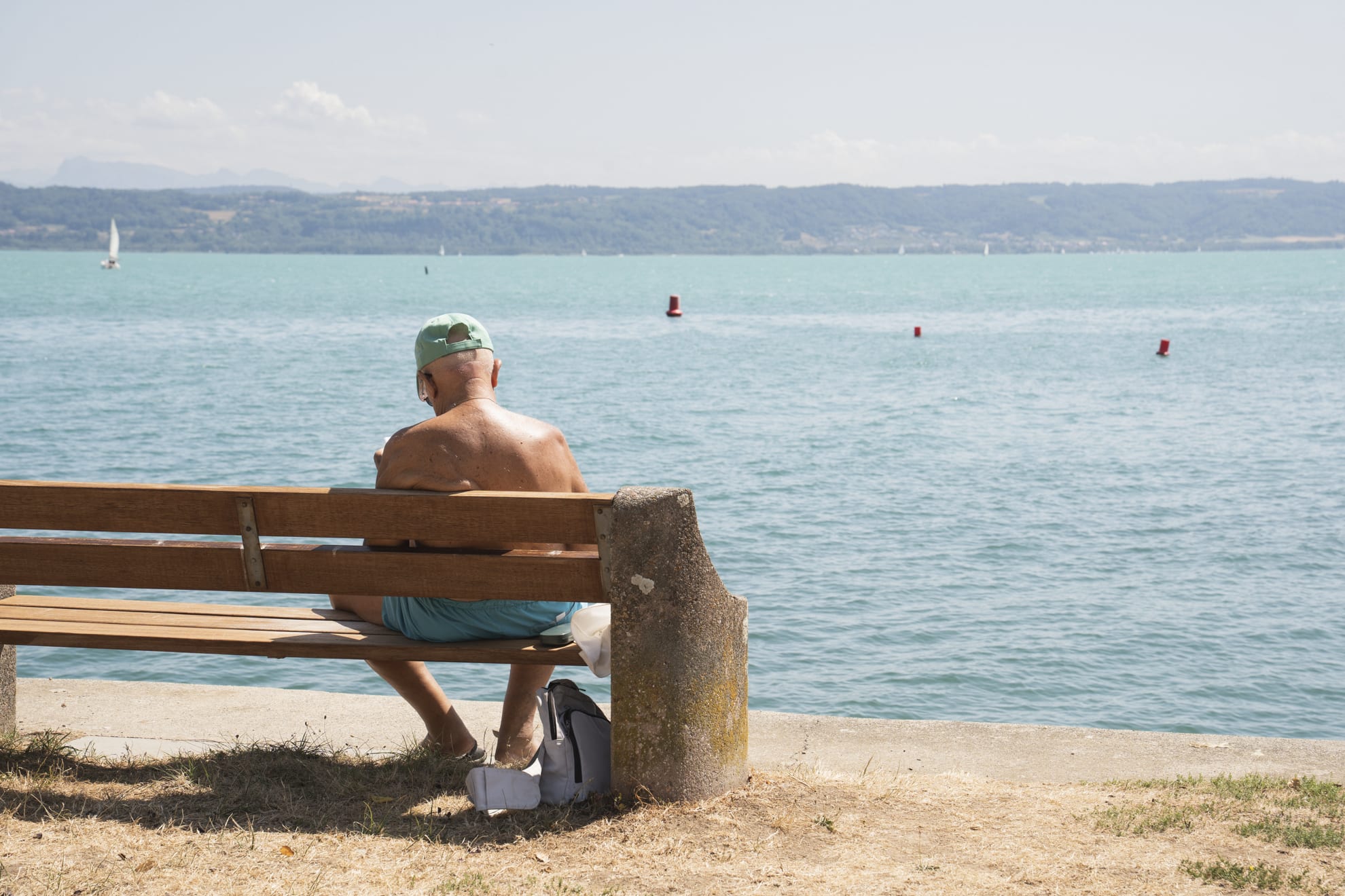 Une personne prend une photo au bord du lac, devant un voilier.
