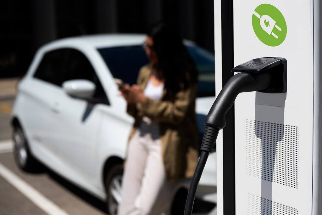 Mujer cargando su coche eléctrico mientras espera