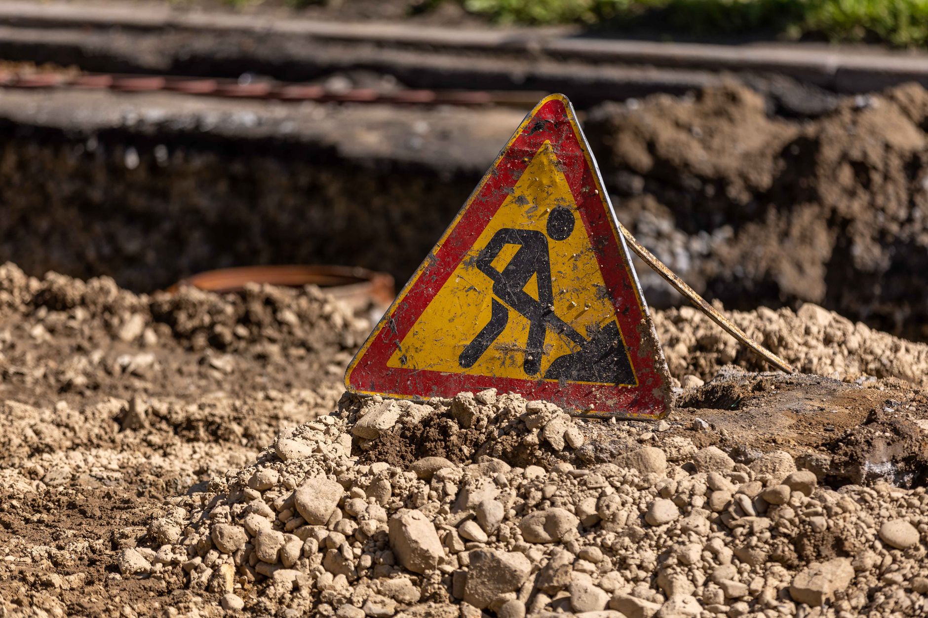 Triangular caution sign at a construction site in a rocky, outdoor setting.