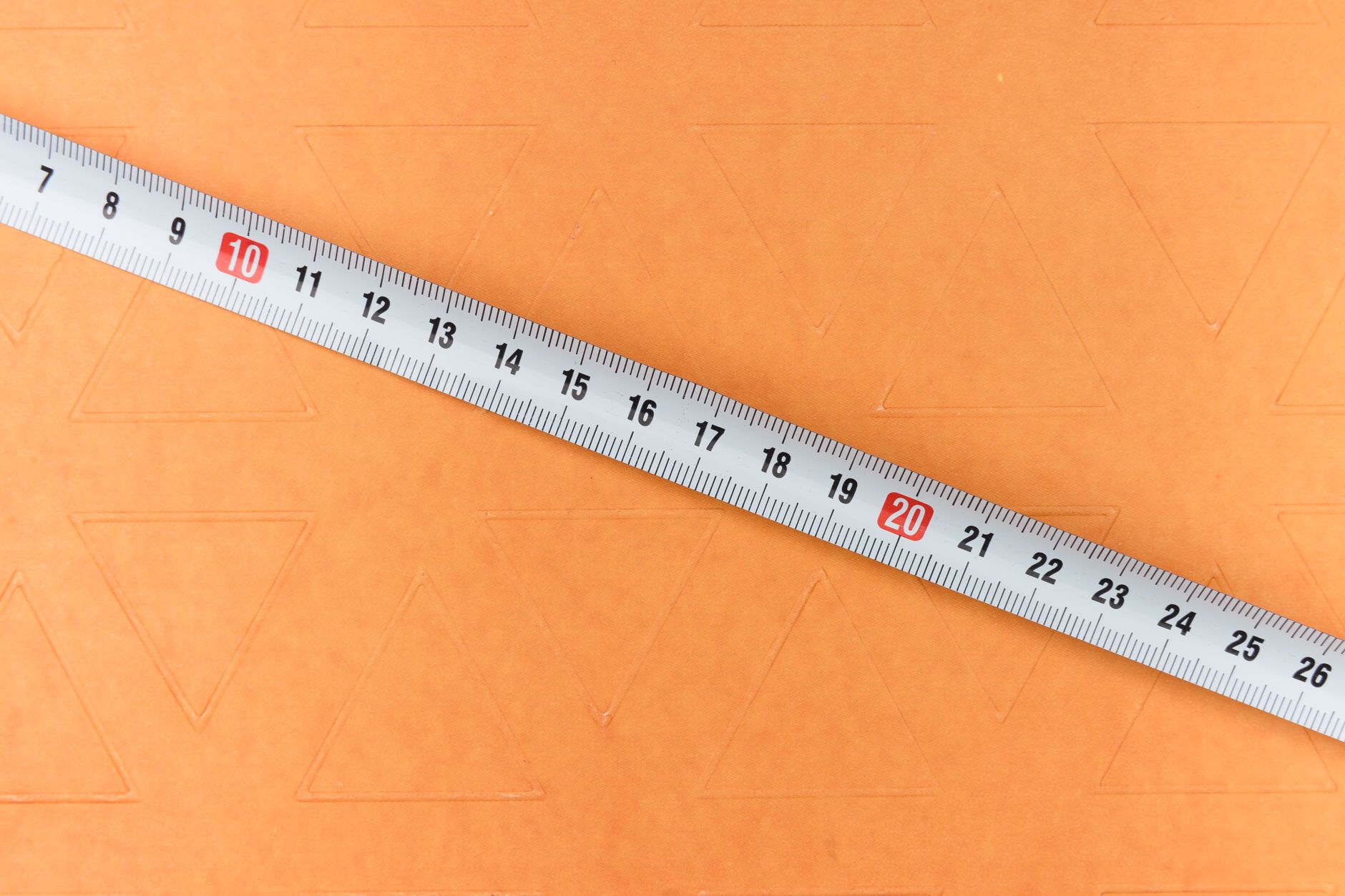 A close-up view of a metal measuring tape diagonally placed on an orange surface.