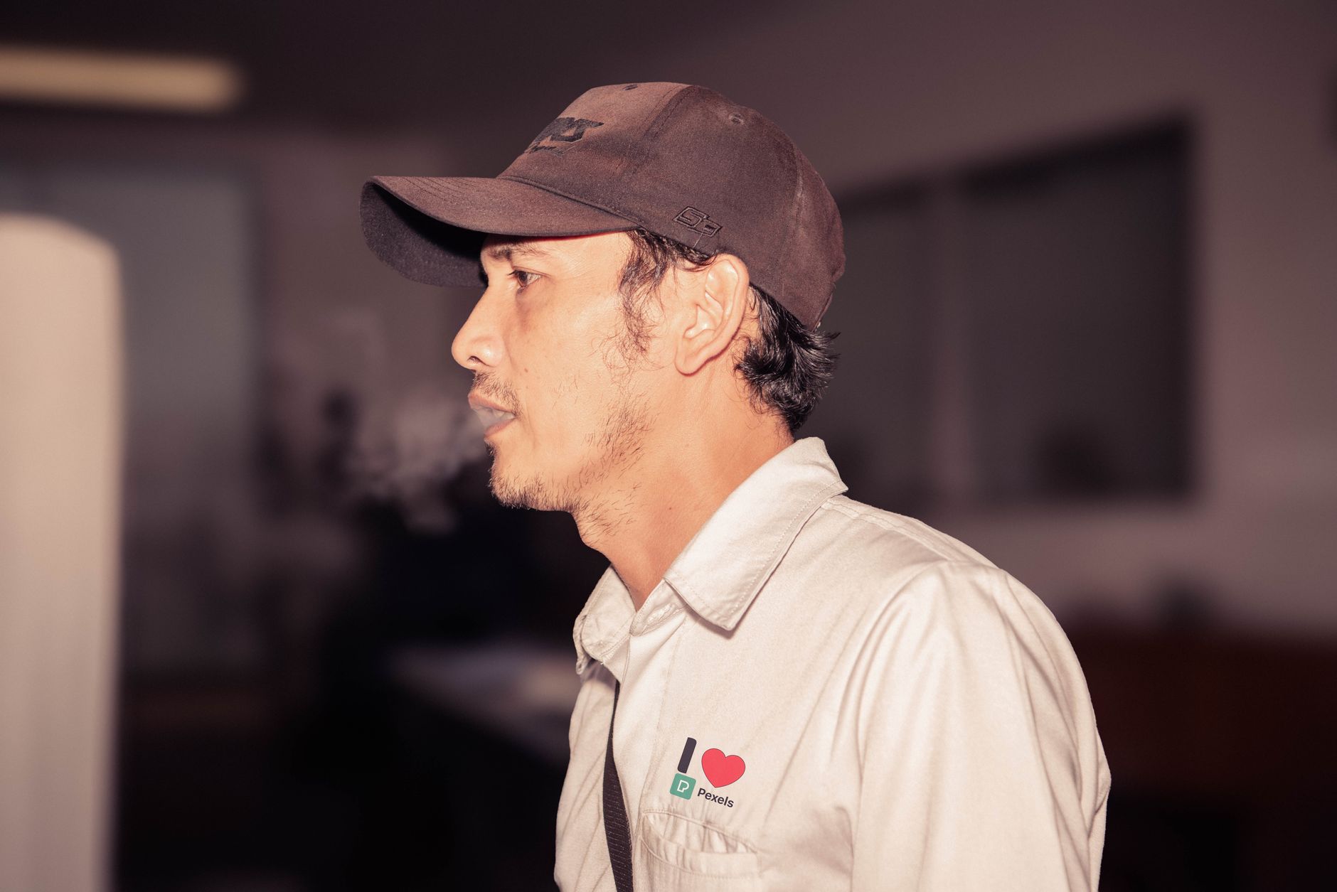 A man in a casual shirt and cap looking to the side in an indoor setting.