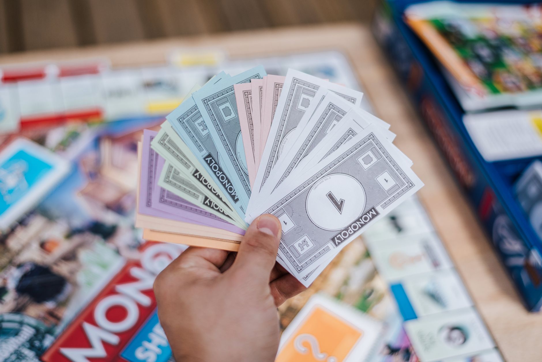 From above of crop anonymous man with collection of fake money playing Monopoly above board