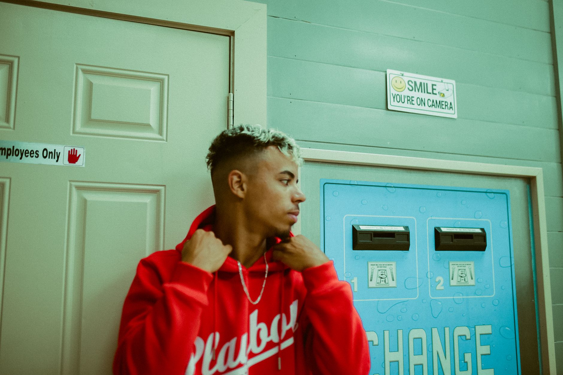 Stylish young adult in red hoodie posing indoors by signage and doors.