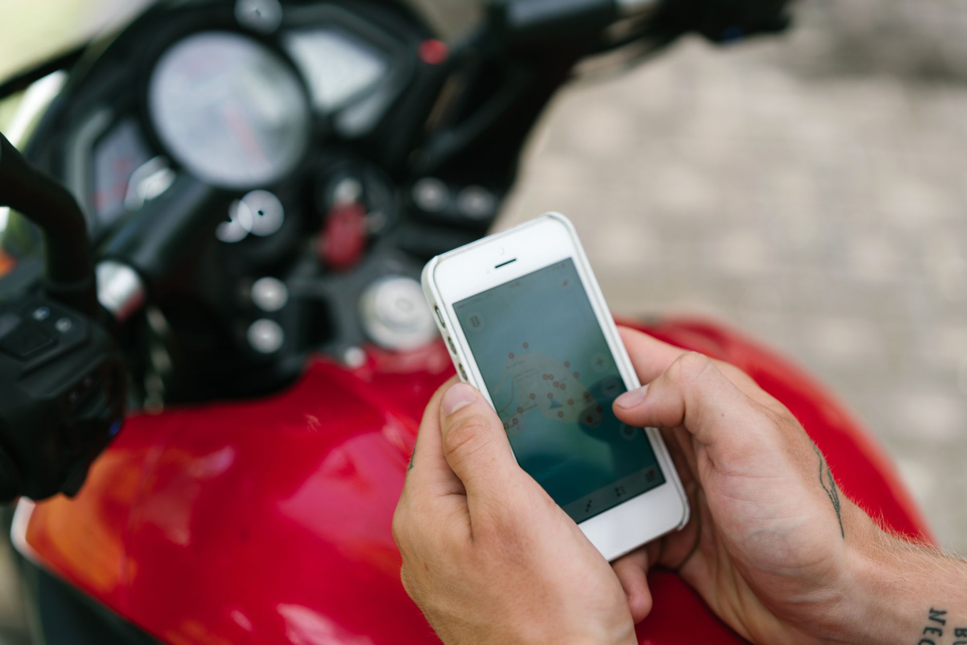 From above of crop unrecognizable tattooed male using smartphone while studying map of city via app in Internet sitting on motorbike on street