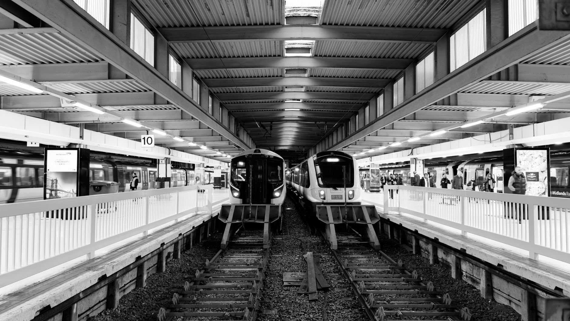Monochrome view of a bustling train station in London, capturing two trains and commuters.