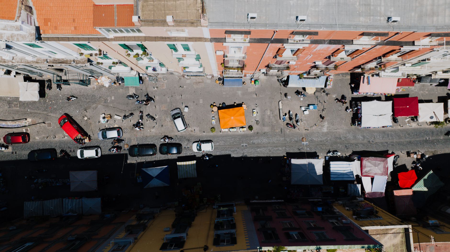 A vibrant aerial shot of a bustling market street in Naples, Italy, showcasing stalls, cars, and urban life.