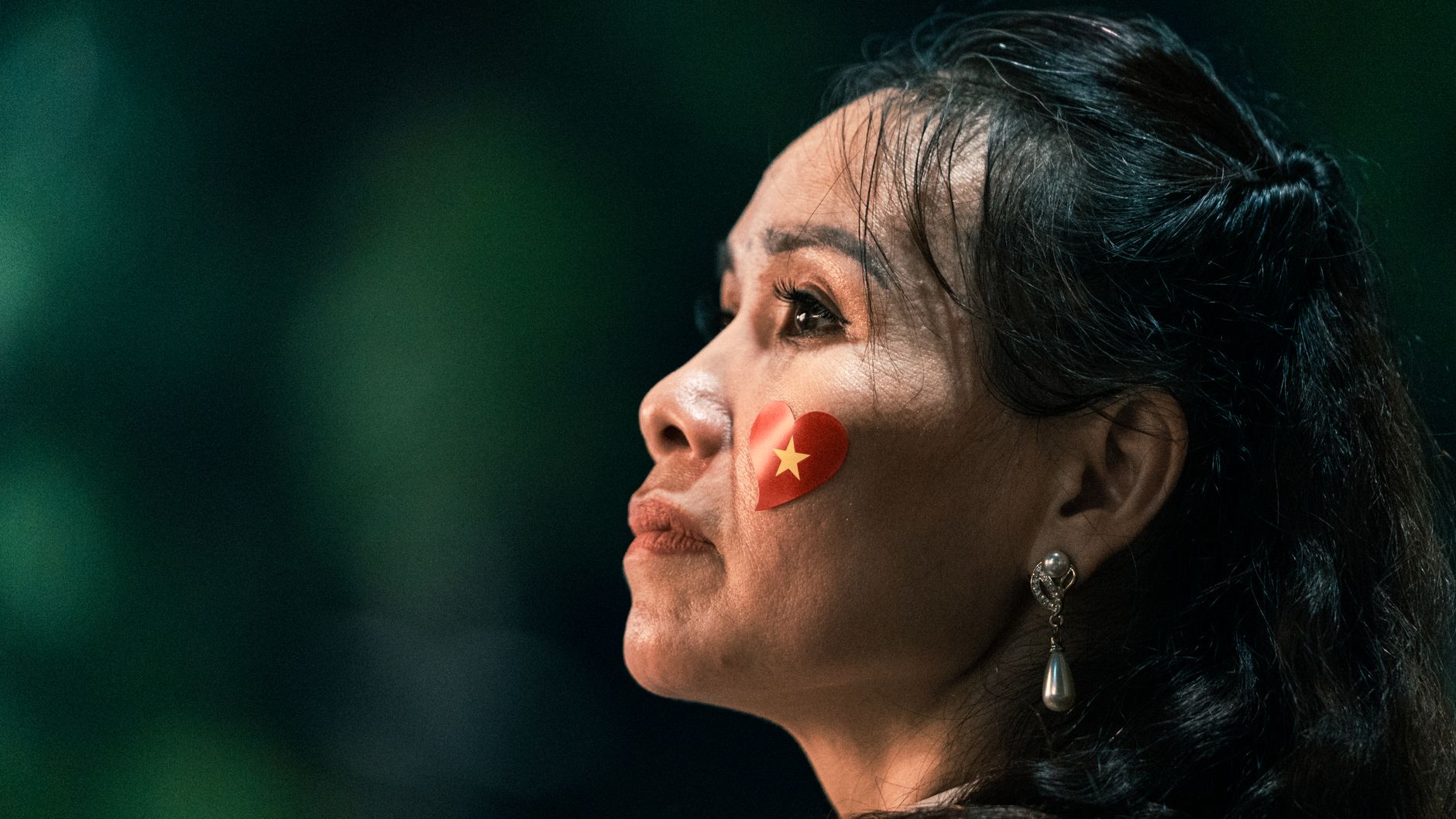 Close-up of a thoughtful woman with a Vietnam flag heart sticker on her cheek.