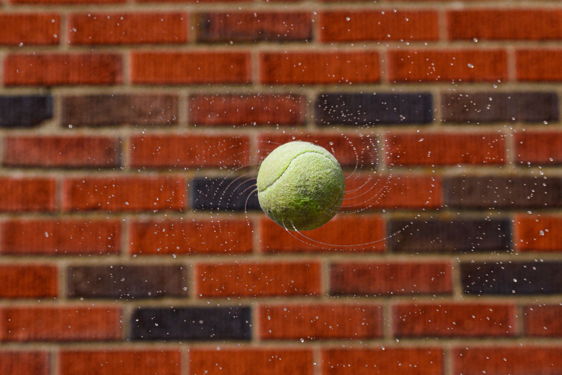 Dynamic tennis ball captured mid-air with water droplets and brick wall backdrop.