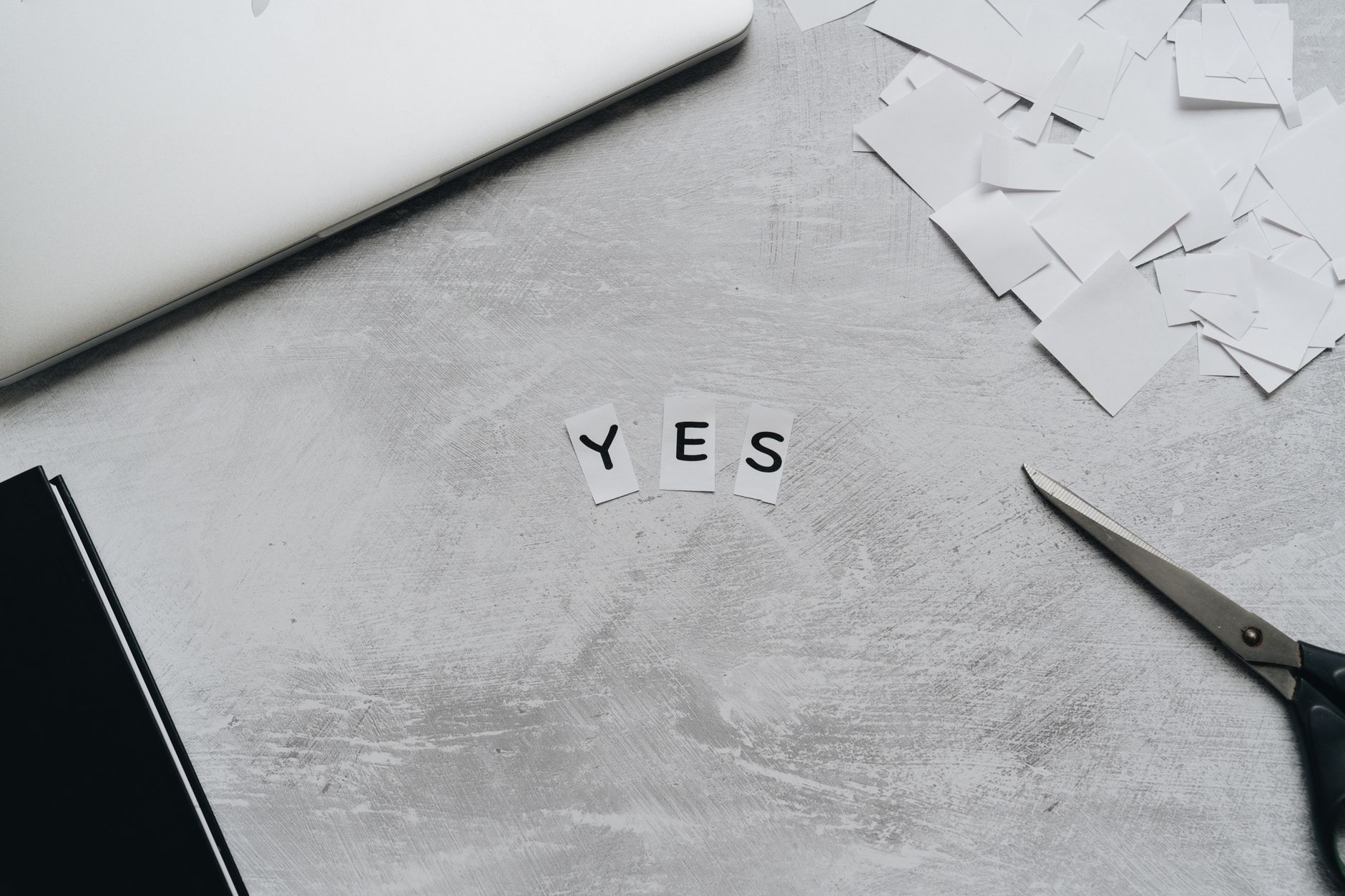 Artistic layout of paper cutouts forming 'YES' with scissors on a desk surface.