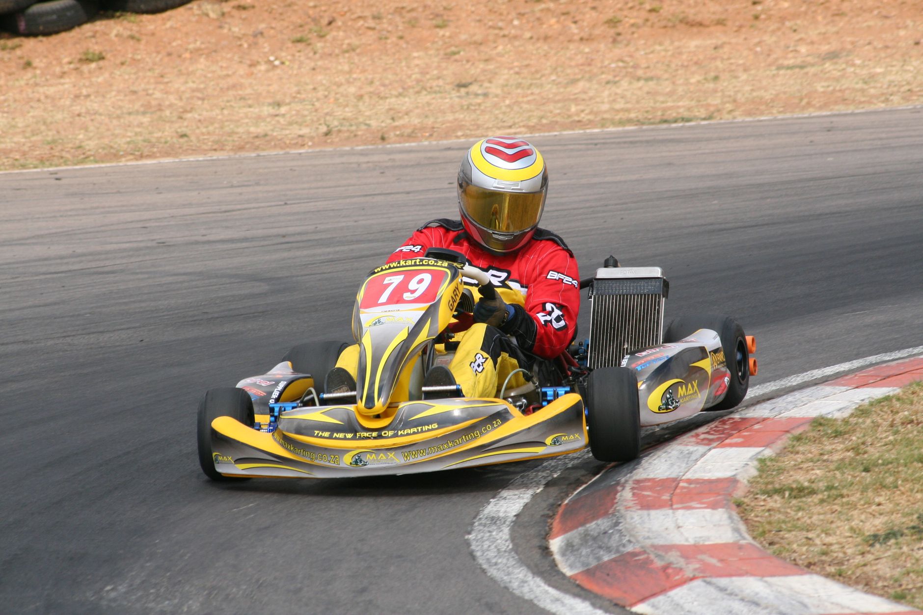 A go-kart racer in vibrant gear speeds around a turn on an outdoor track.