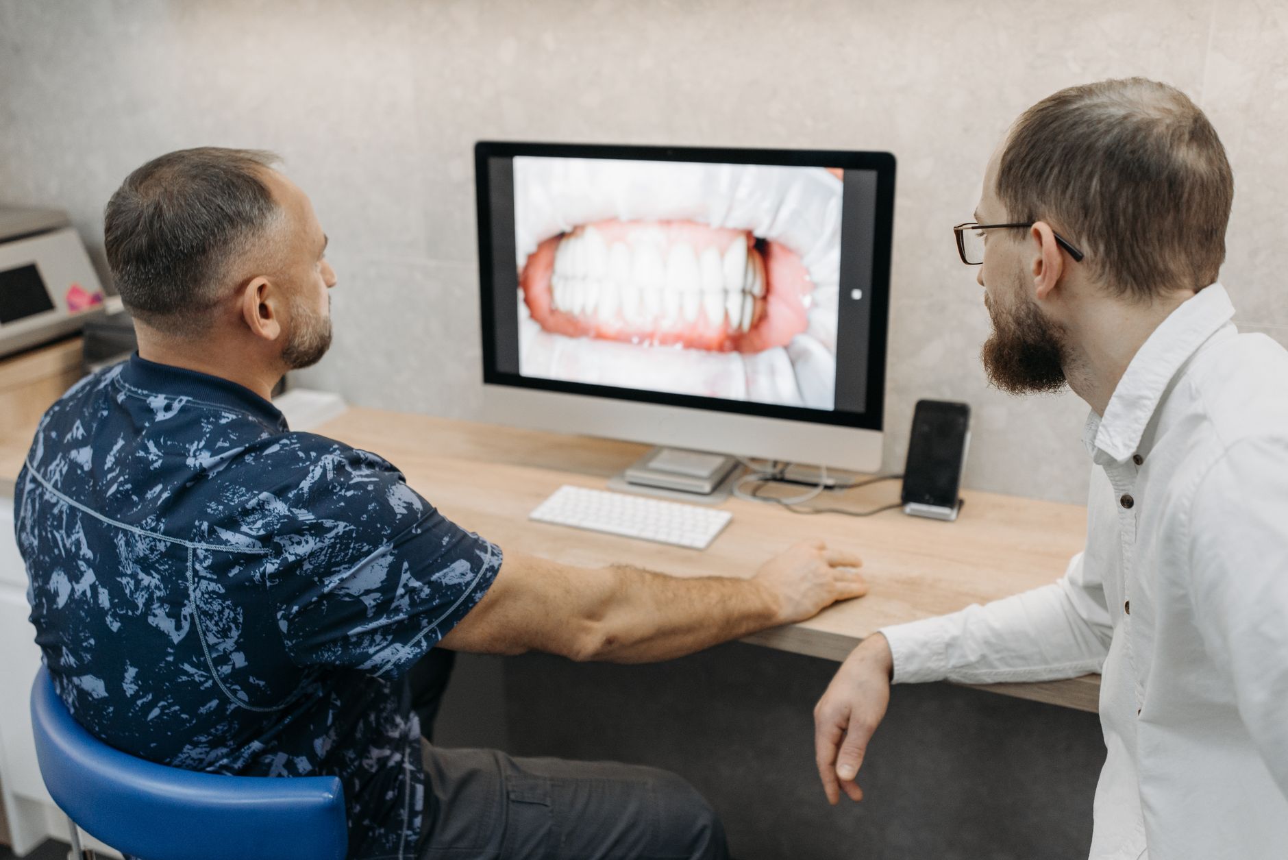 Two male dentists observe dental images on a computer screen in a clinic.